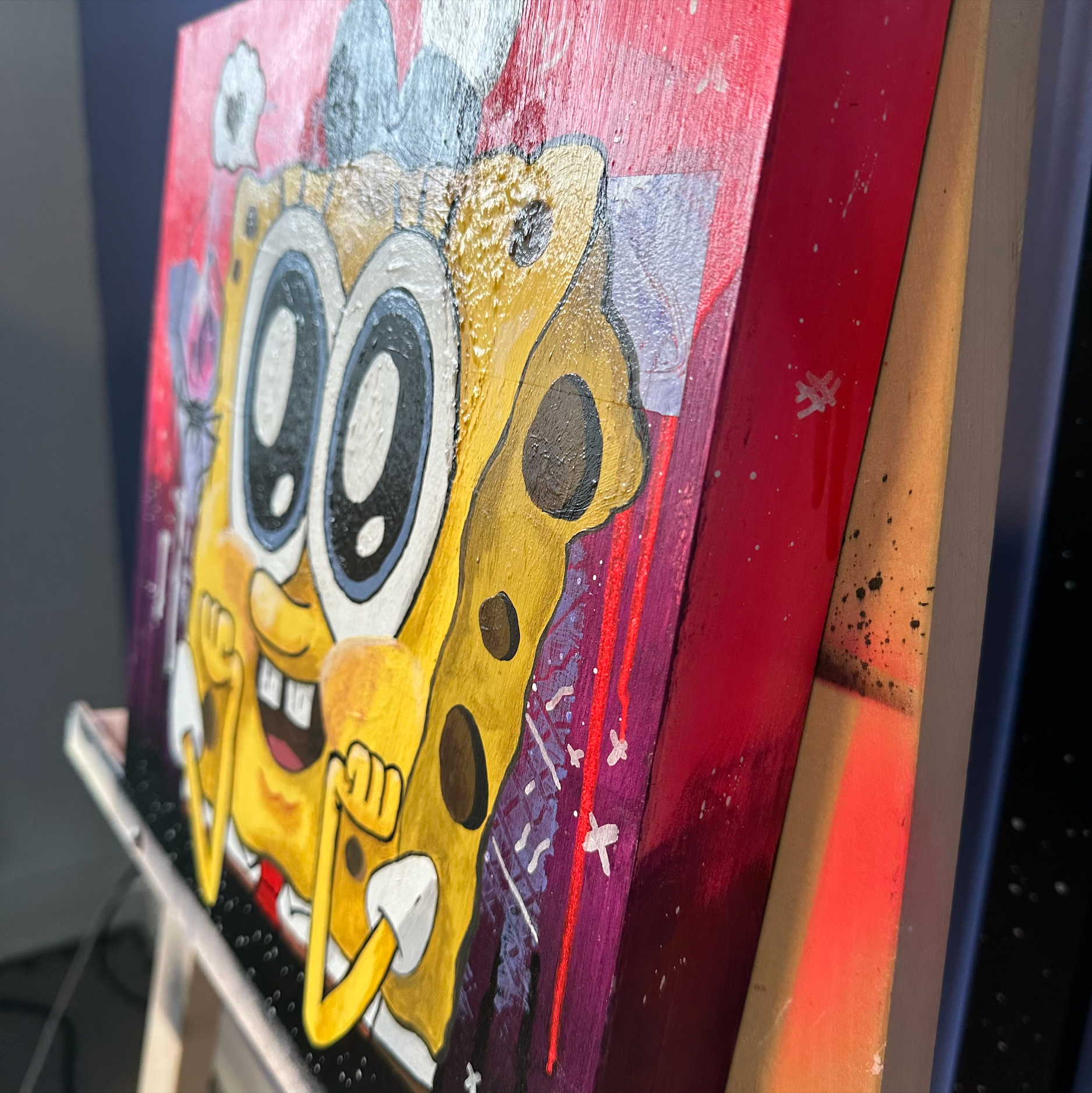 Right side view of an acrylic painting on wood canvas made by the artist Catherine Barletta. showing a weird love between SpongeBob and a shinny crystal spider